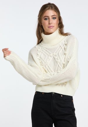 Strickpullover in Off-White mit hohem Rollkragen. Verfügt über strukturierte Muster und gerippte Bündchen, getragen mit schwarzen Jeans.