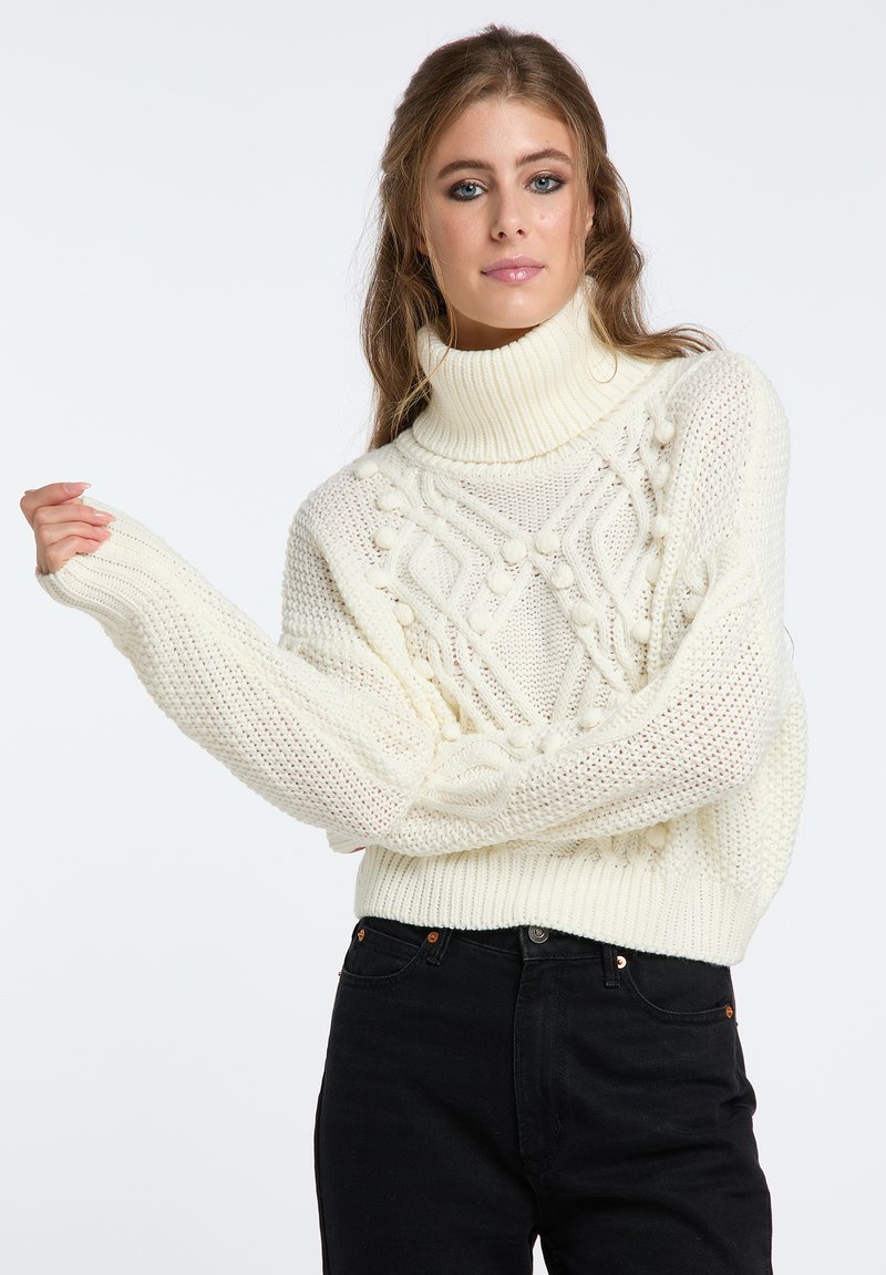 Strickpullover in Off-White mit hohem Rollkragen. Verfügt über strukturierte Muster und gerippte Bündchen, getragen mit schwarzen Jeans.