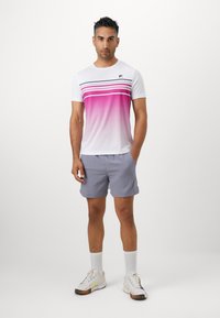 Herren T-Shirt mit kurzen Ärmeln im Farbverlauf von Weiß zu Pink, mit horizontalen Streifen, kombiniert mit hellgrauen Shorts und weißen Sneakers.