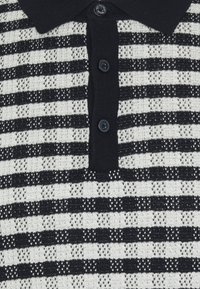 Polo tricoté en noir et blanc avec des rayures horizontales et une patte de boutonnage noire comportant trois boutons ronds noirs.