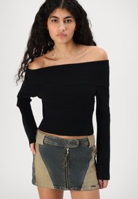 Svart av-shoulder ribbestrikket topp kombinert med en lappekreasjon i denim miniskjørt med glidelås og kontrasterende stoffseksjoner.