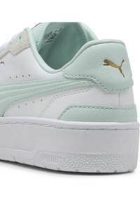 Bílé tenisky s mátově zelenými akcenty, vyrobené z kůže a semiše, s texturovanými detaily, zlatým logem, hladkým povrchem a gumovou podrážkou.