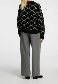 Svart stickad tröja med vitt diamantmönster, tillsammans med grå vida byxor och svarta platta skor. Vy bakifrån.
