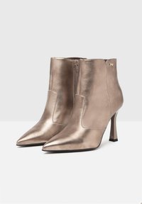 Bottes de cheville en bronze métallique avec un bout pointu, un talon stiletto fin et une fermeture éclair sur le côté. Texture lisse avec des accents minimaux.