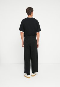 Black short-sleeve T-shirt with white trim, paired with wide-leg black pants and white shoes with a gum sole, viewed from the back.