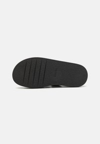 Semelle de chaussure en caoutchouc noir avec une finition texturée, présentant des rainures horizontales pour une traction et une forme arrondie.