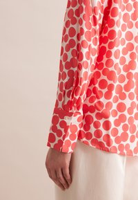 Blusa rossa e bianca con motivo a pois, maniche lunghe con polsini abbottonati e vestibilità comoda. Realizzata in tessuto leggero.