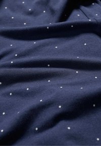 Tumesinine puuvillane kangas valgete näppudega, millel on sile tekstuur ja pehme langevus, näidates õrnu voldikuid ja kortse.