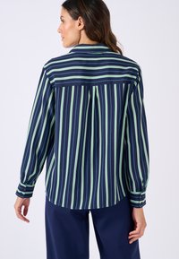 Chemise bleu marine à rayures comportant des rayures horizontales et verticales vertes. Manches longues avec poignets à boutons, coupe décontractée, détail de empiècement au dos.