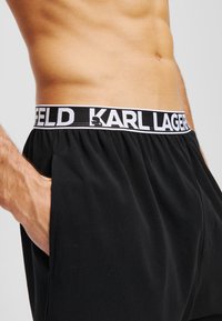 Zwarte shorts met een zachte textuur hebben een contrasterende witte tailleband met de tekst "KARL LAGERFELD", ontworpen voor comfort en stijl.