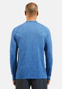 Blauwe sportieve shirt met lange mouwen, gemaakt van een textuurstof, met een ronde hals en raglanmouwen, ontworpen voor comfort en mobiliteit.