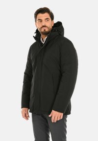 Giacca nera isolata con zip frontale, cappuccio regolabile, tasche laterali e una consistenza elegante e liscia.