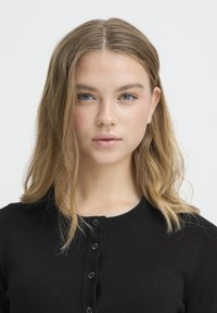 Črni kardigan z okroglim izrezom in zapiranjem na gumbe. Mehka tekstura, oprijeta zasnova in gladka tkanina z rahlo opaznim sijajem.