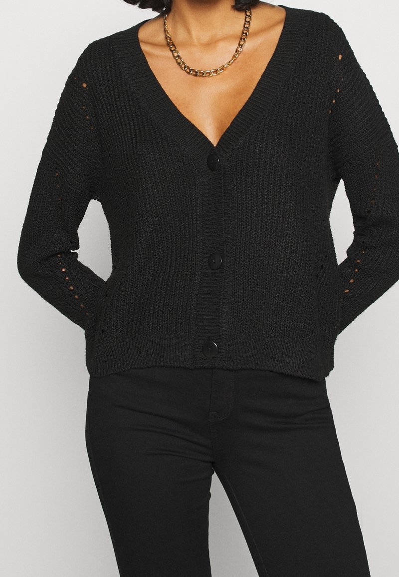 Czarny dziergany kardigan z głębokim dekoltem w kształcie litery V, czterema guzikami i ażurowym detalem na rękawach. Teksturowana tkanina z prążkowymi krawędziami.