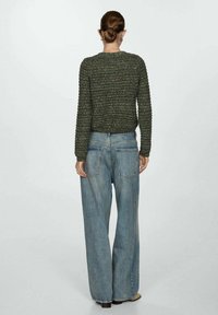 Pull en maille texturée verte avec un col rond, associé à un jean bleu clair ample avec des poches arrière.