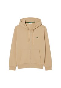 Sudadera con capucha y cremallera en beige, hecha de tela suave, con un bolsillo tipo canguro, capucha con cordón y un pequeño logo verde en el pecho izquierdo.