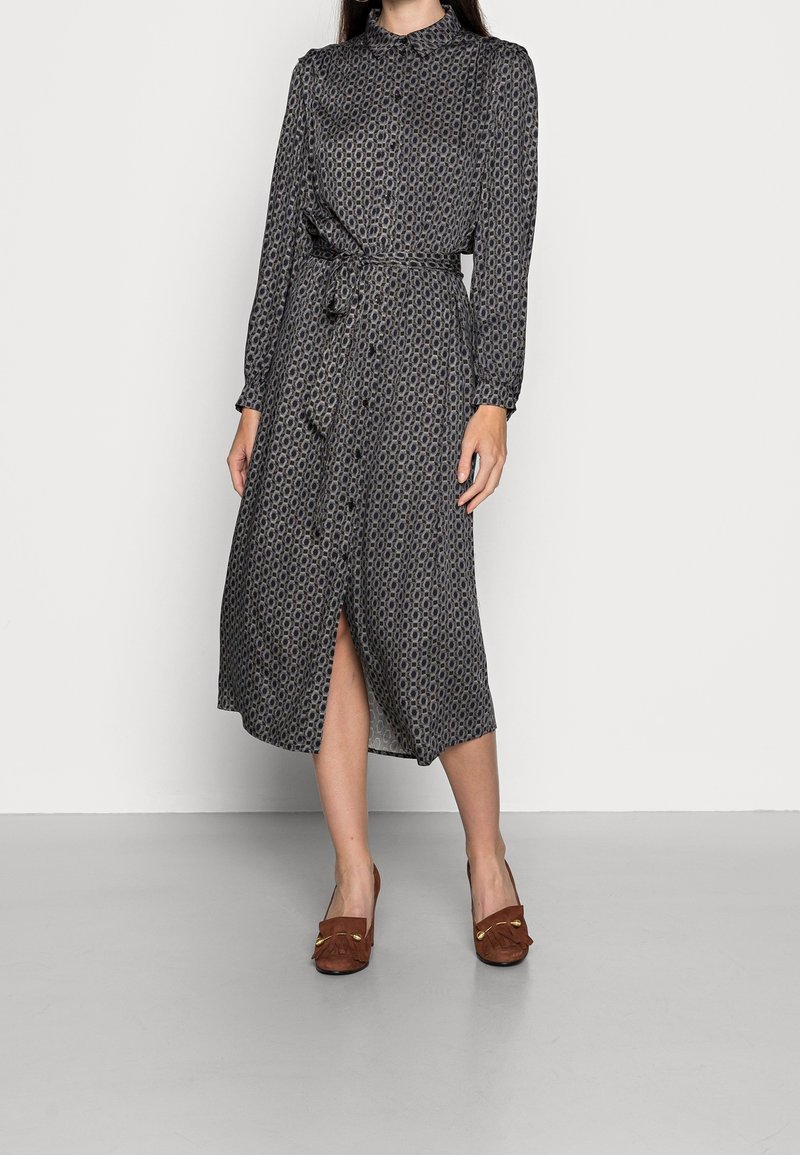 Femme portant une robe chemise midi à manches longues à motifs avec une ceinture à la taille et des mocassins en daim marron avec des accents dorés.