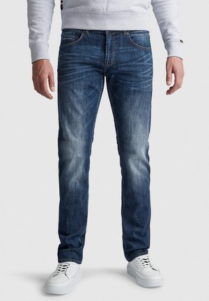 Jeans di denim blu scuro con dettagli sbiaditi, taglio dritto, design a cinque tasche e cuciture a contrasto. Indossati con sneakers bianche.