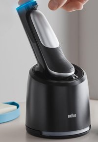 Rasoir électrique avec une base noire élégante, un manche argenté et une prise texturée. Comprend un indicateur LED bleu sur le dessus pour la fonctionnalité.