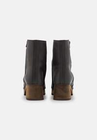 Černé kožené kotníkové boty s dřevěnými blokovými podpatky, které mají hladkou texturu, vertikální švy a postranní zip.