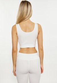 Weißes Sport-Crop-Top mit rundem Halsauschnitt, tailliertem Schnitt und glatter Textur, kombiniert mit passenden hoch geschnittenen Leggings.