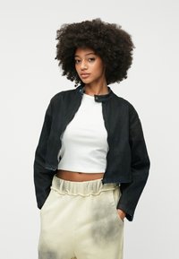 Crna traper bomber jakna s kratkim dizajnom, uspravnim ovratnikom i zatvaranjem na patentni zatvarač, uparen je s svijetlosmešavim hlačama koje imaju efekt izbljeđenja.