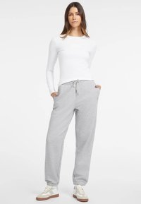 Pantaloni felpa grigi con polsini ed elastico in vita, abbinati a una maglietta bianca a manica lunga. Le scarpe presentano una combinazione di colori beige e bianco.