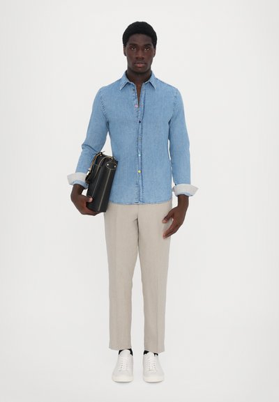 Light denim button-up shirt with colorful buttons, beige linen trousers, and white sneakers. Black bag accented with gold detailing.