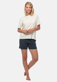 Lichtbeige katoenen t-shirt met korte mouwen, gecombineerd met marineblauwe gestreepte shorts met witte verticale lijnen, tot halverwege de dijen.