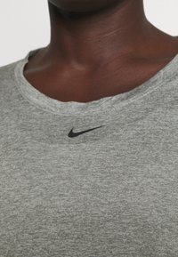 Harmaa urheilu t-paita, joka on valmistettu teksturoidusta kankaasta ja jossa on musta Nike-logo rinnassa sekä leveä, pyöreä kaula-aukko.