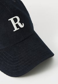 Casquette de baseball en velours côtelé bleu marine avec un "R" brodé en blanc à l'avant, dotée d'une visière courbée et d'un tissu texturé.