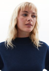 Maglione blu navy con un alto col ribattuto, tessuto morbido e una vestibilità rilassata, senza motivi visibili o dettagli in metallo.