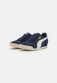 Zapatillas deportivas de color azul marino con una franja blanca a los lados, tela texturizada, cordones redondeados y una suela de goma beige con un patrón estriado.