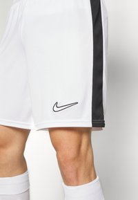 Vita atletiska shorts med svarta sidopaneler, med sydd fåll och en svart Nike-logotyp på vänster ben. Slät, lättviktsmaterial.