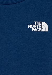 Sweatshirt azul feito de tecido suave, apresentando um logótipo branco da "The North Face" no lado esquerdo do peito, com um decote redondo e acabamento texturizado.