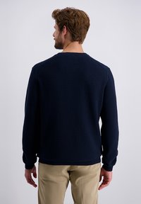 Navy blauwe, gestructureerde gebreide trui met lange mouwen en een ronde halslijn, gecombineerd met beige broek. De achteraanzicht benadrukt het patroon van de stof.