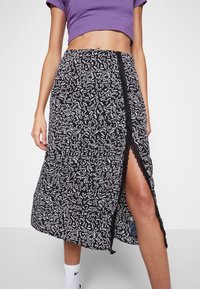 Jupe à motifs noir et blanc avec un ourlet asymétrique, dotée d'une fente sur le côté et d'une finition en dentelle, fabriquée à partir d'un tissu léger.
