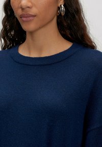 Marineblaues Sweatshirt mit rundem Ausschnitt, strukturiertem Strickstoff und gerippten Bündchen, kombiniert mit glänzenden silbernen Creolen.