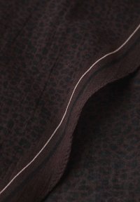 Tissu brun foncé avec un motif léger de léopard et un bord replié présentant de fines rayures contrastées claires et foncées.