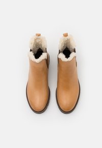 Bottes cheville en cuir fauve avec une doublure en fourrure en haut et un intérieur noir. Dotées d'une petite languette pour faciliter l'enfilage et d'une forme à bout rond.