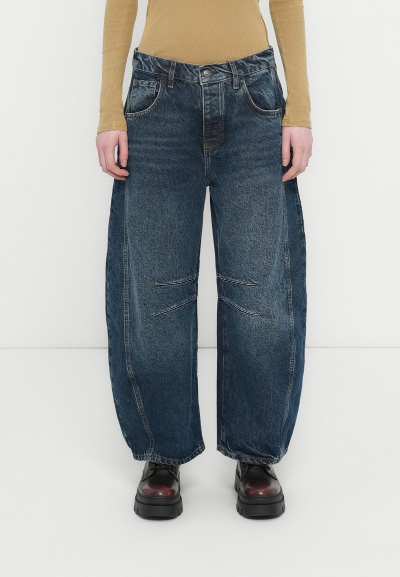 Μπλε τζιν παντελόνι με φαρδιά πόδια και ξεθωριασμένο φινίρισμα, με διπλές μπροστινές τσέπες, ορατές ραφές και διακοσμητικές εγκοπές στα γόνατα.