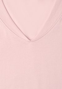 T-shirt rose clair à col en V montrant la texture du tissu et les détails des coutures autour de l'encolure.