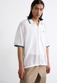 Hvit nettstoff kortermet skjorte med lys grønn krage og mansjetter, med knappelukking og liten logo på venstre bryst.