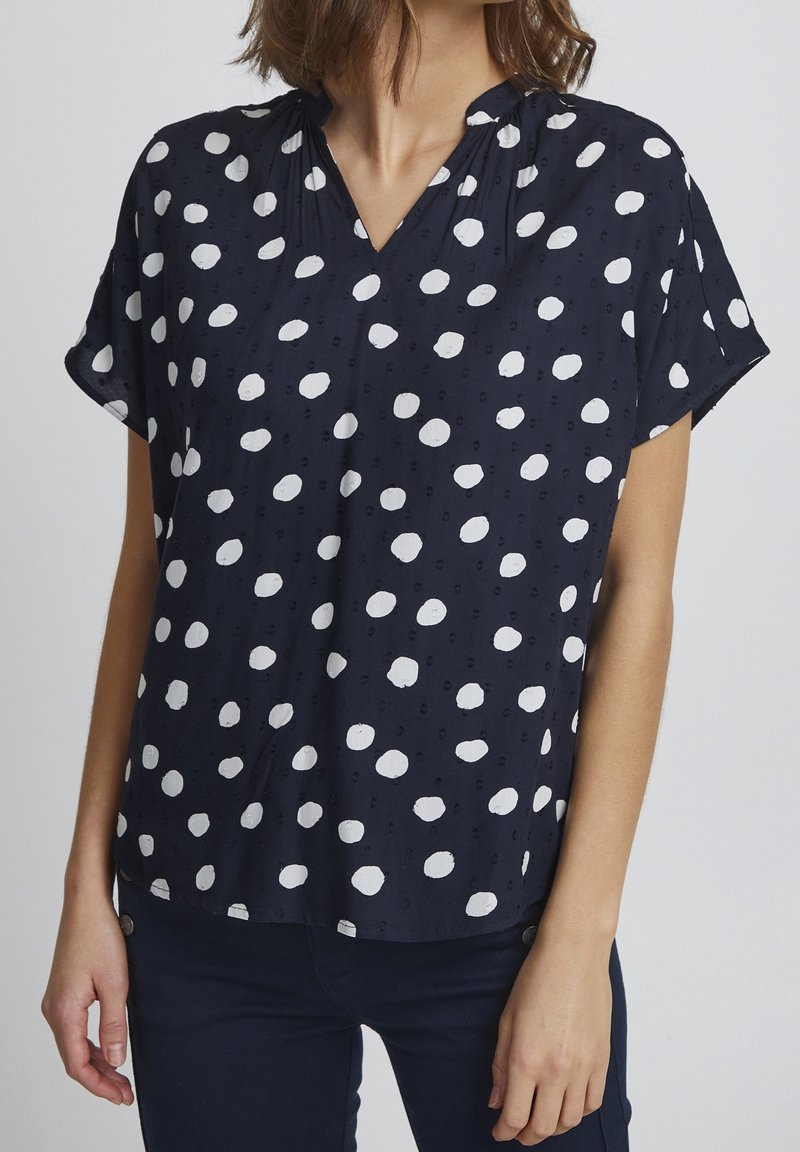 Navy top with white polka dots, short sleeves, and a V-neck design. Features subtle texture and a relaxed fit.