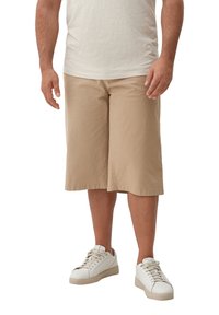 Beige knielange shorts van lichtgewicht stof, met een relaxte pasvorm en soepele textuur, gecombineerd met witte sportschoenen.