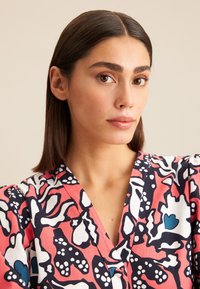 Sukienka w kwiatowy wzór z różowymi, granatowymi i białymi kolorami. Dekolt w kształcie litery V, teksturowany materiał oraz bufiaste rękawy.