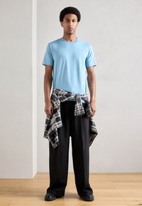 Világoskék rövid ujjú póló kerek nyakkivágással, laza fekete nadrággal és deréknál megkötött fekete-fehér kockás inggel párosítva.