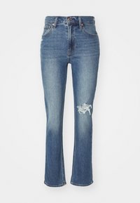 Blue denim jeans with a flared hem, high waist, slight distressing on the left knee, and traditional five-pocket design.