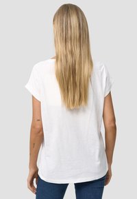 Hvid kortærmet top i letvægtsstof med en let afslappet pasform og rundet kant, parret med mørkeblå jeans.
