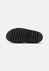 Black rubber shoe sole with horizontal grooves, textured design, and a rounded toe. Features a brand logo in the center.